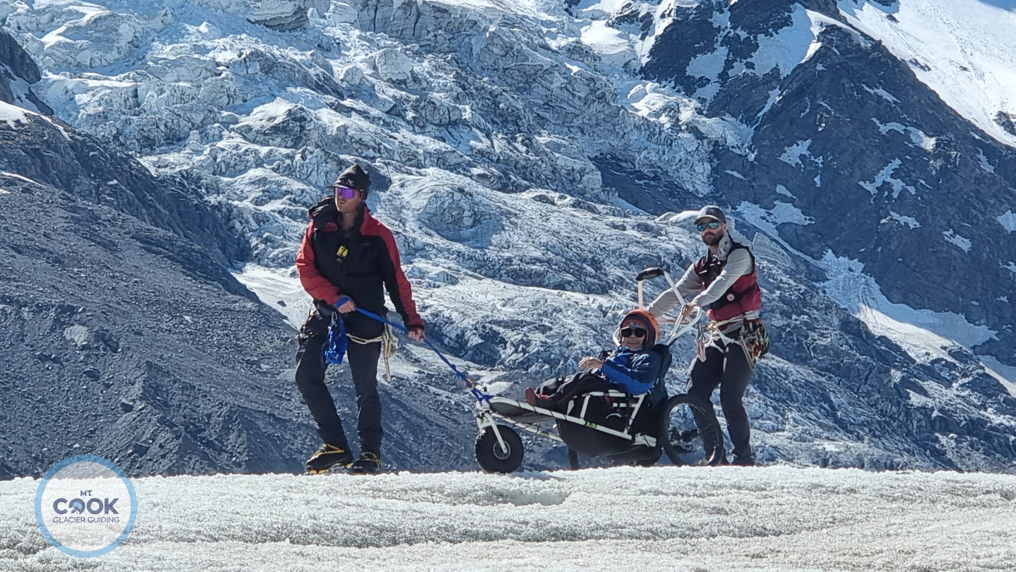 The feature photo is the Tasman Glacier with a person being guided by two guides. The client is in a adaptive buggy. A specialized buggy that the MakingTrax Foundation provides in the Mount Cook Glacier Guides listing.